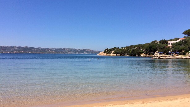 A beach with clear water, a sandy shore, and a building on a hill.