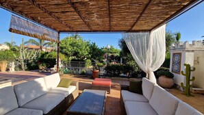 Une terrasse extérieure aménagée avec des meubles en osier, une table en verre et un cactus décoratif.