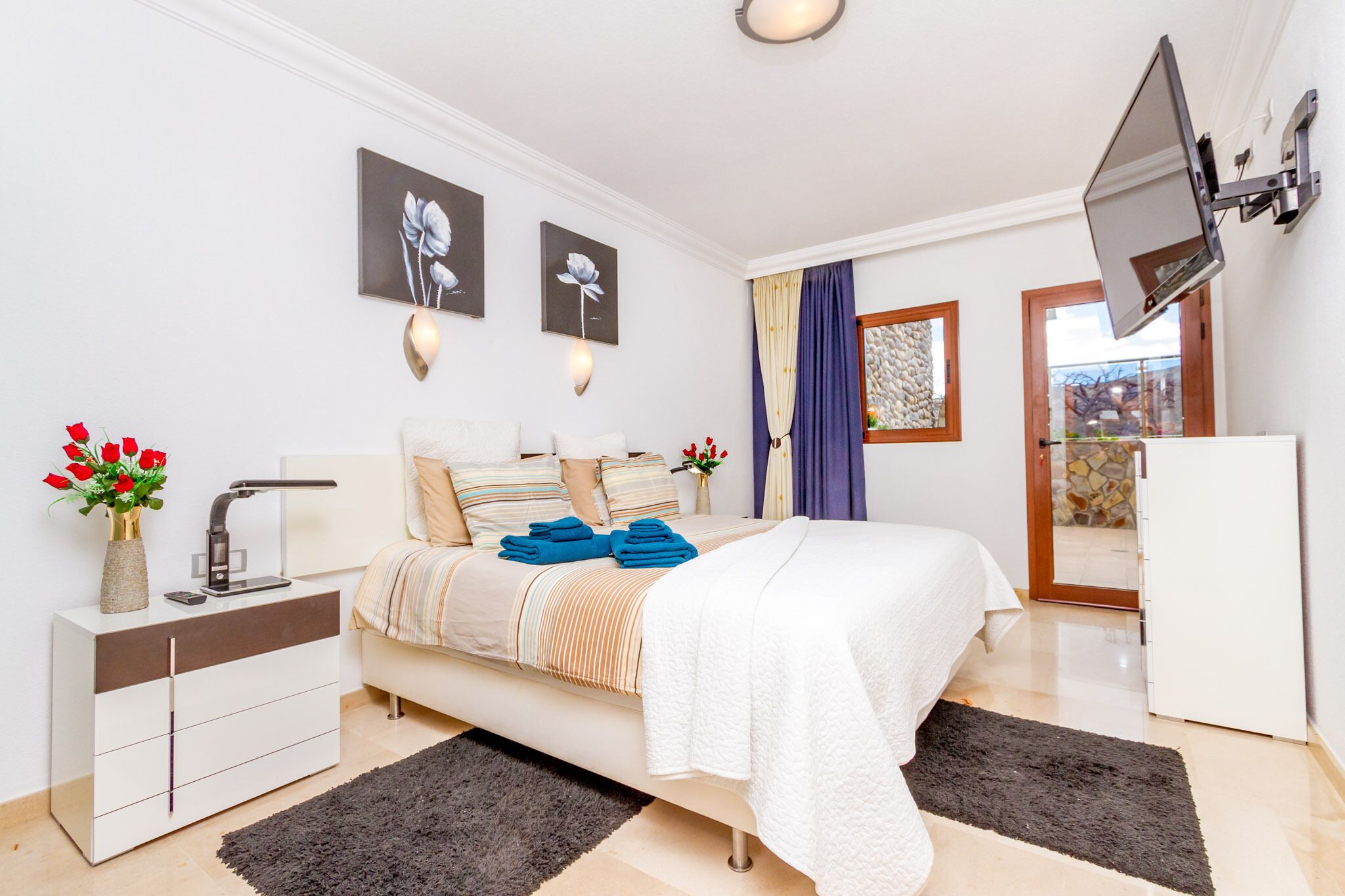 A modern bedroom with a bed, bedside table, TV, and artwork on the wall.