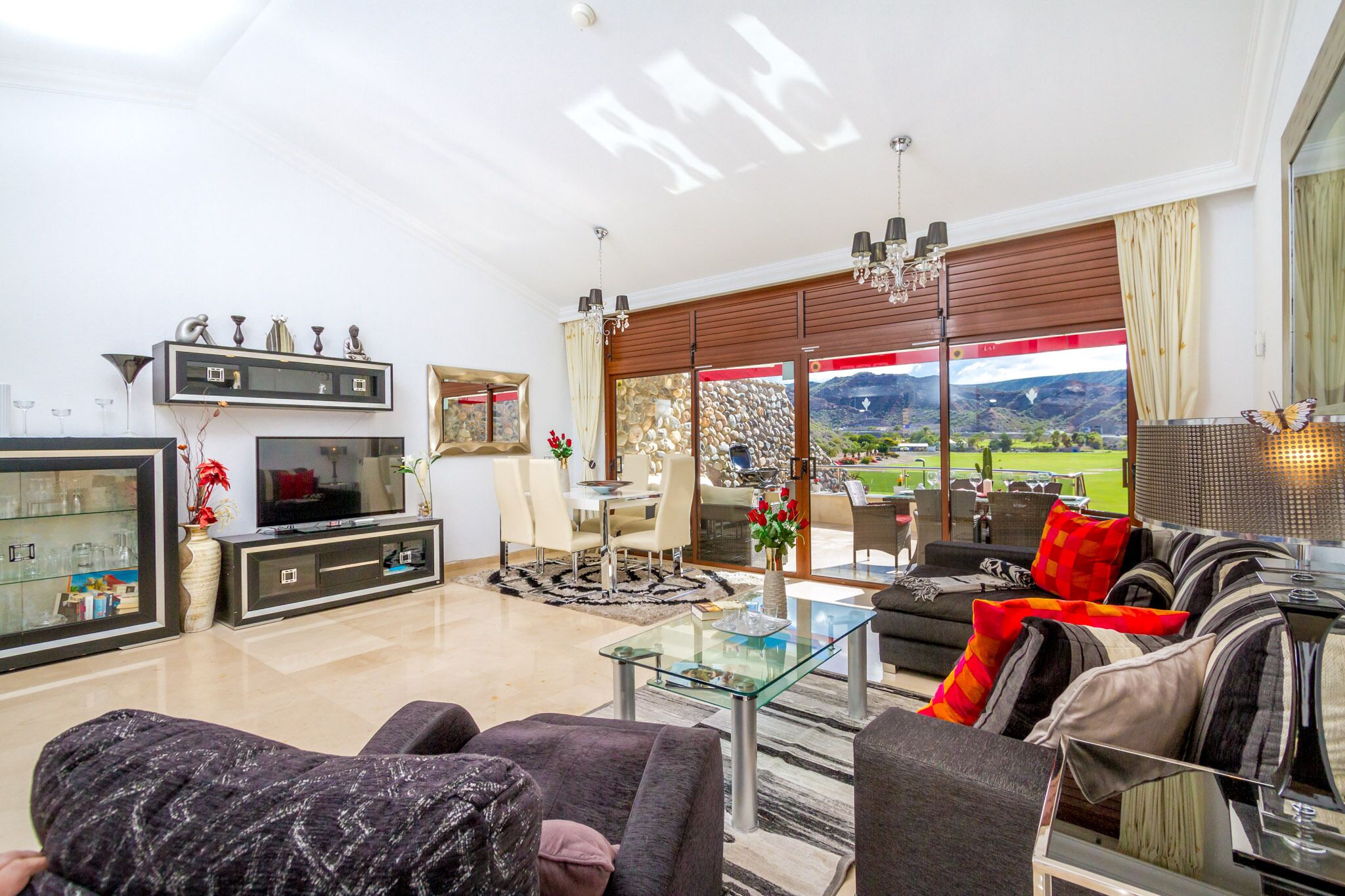 Een moderne woonkamer met een glazen salontafel, comfortabele zithoek, een flatscreen televisie en een prachtig uitzicht door grote ramen.