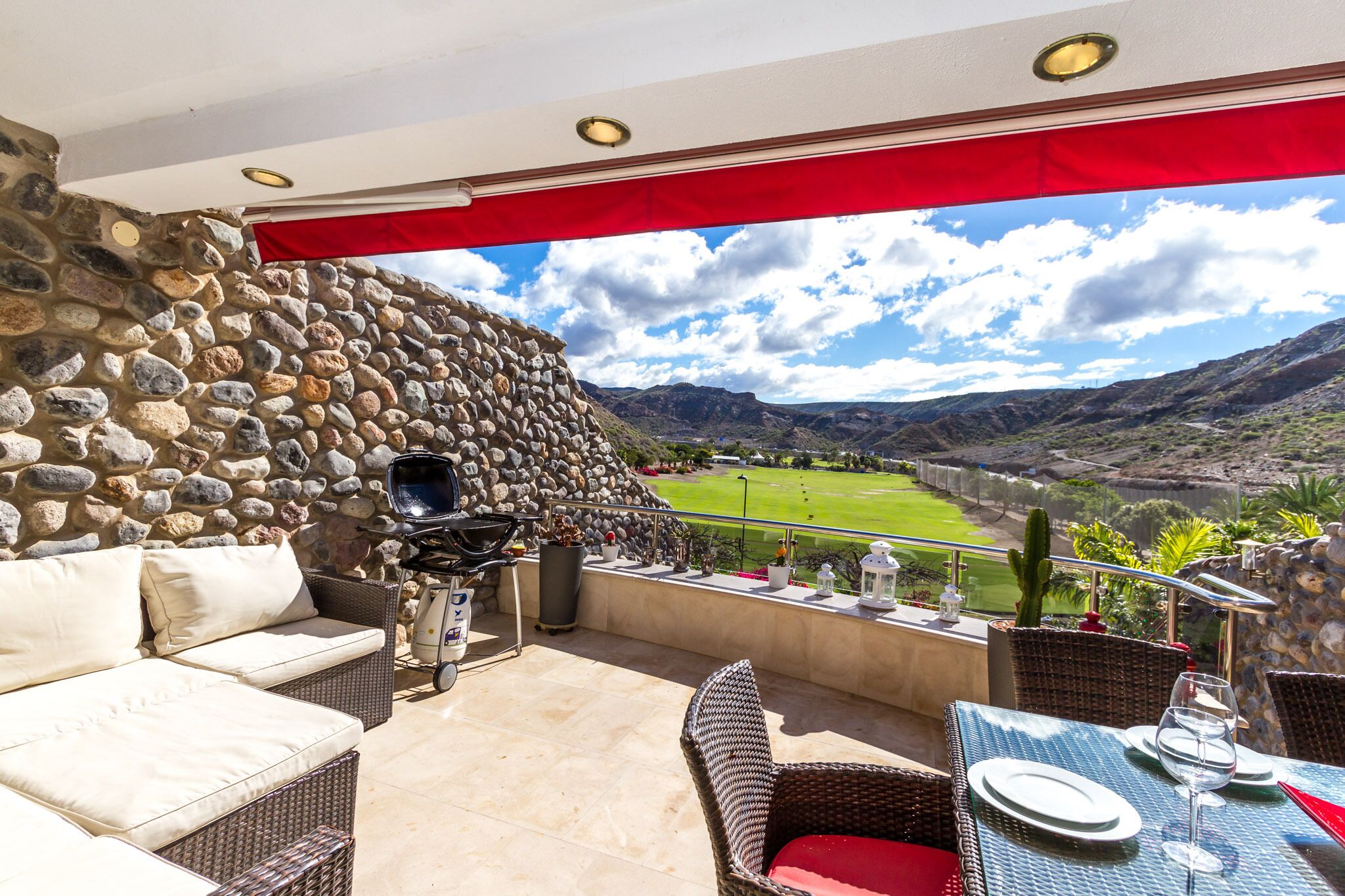 Un patio con mobiliario de mimbre, una pared de piedra y vistas a un valle.