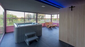 Ein moderner Spa-Bereich mit Whirlpool, Holzliegestühlen und großen Fenstern mit Blick ins Freie.
