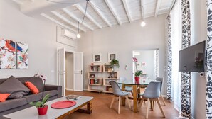 A modern living room with a sofa, coffee table, and dining area. There is a bookshelf and a TV mounted on the wall. - Grotta Pinta 3 | Spacious and elegant just few steps from Piazza Navona (Roma)