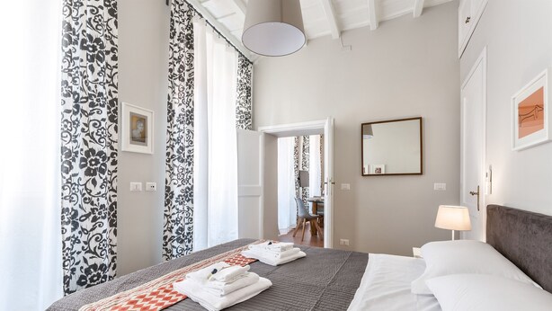 A neatly made bed with towels, a bedside lamp, and a framed picture on the wall. - Grotta Pinta 3 | Spacious and elegant just few steps from Piazza Navona (Roma)