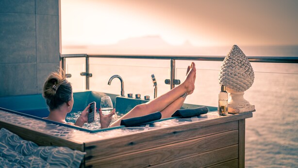 A person relaxing in a wooden bathtub with a view of the ocean and mountains in the background. - Last Minute-Jacuzzi & Sea View (Trabia)