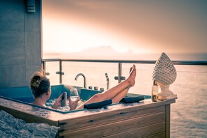 A person relaxing in a wooden bathtub with a view of the ocean and mountains in the background. - Last Minute-Jacuzzi & Sea View (Trabia)