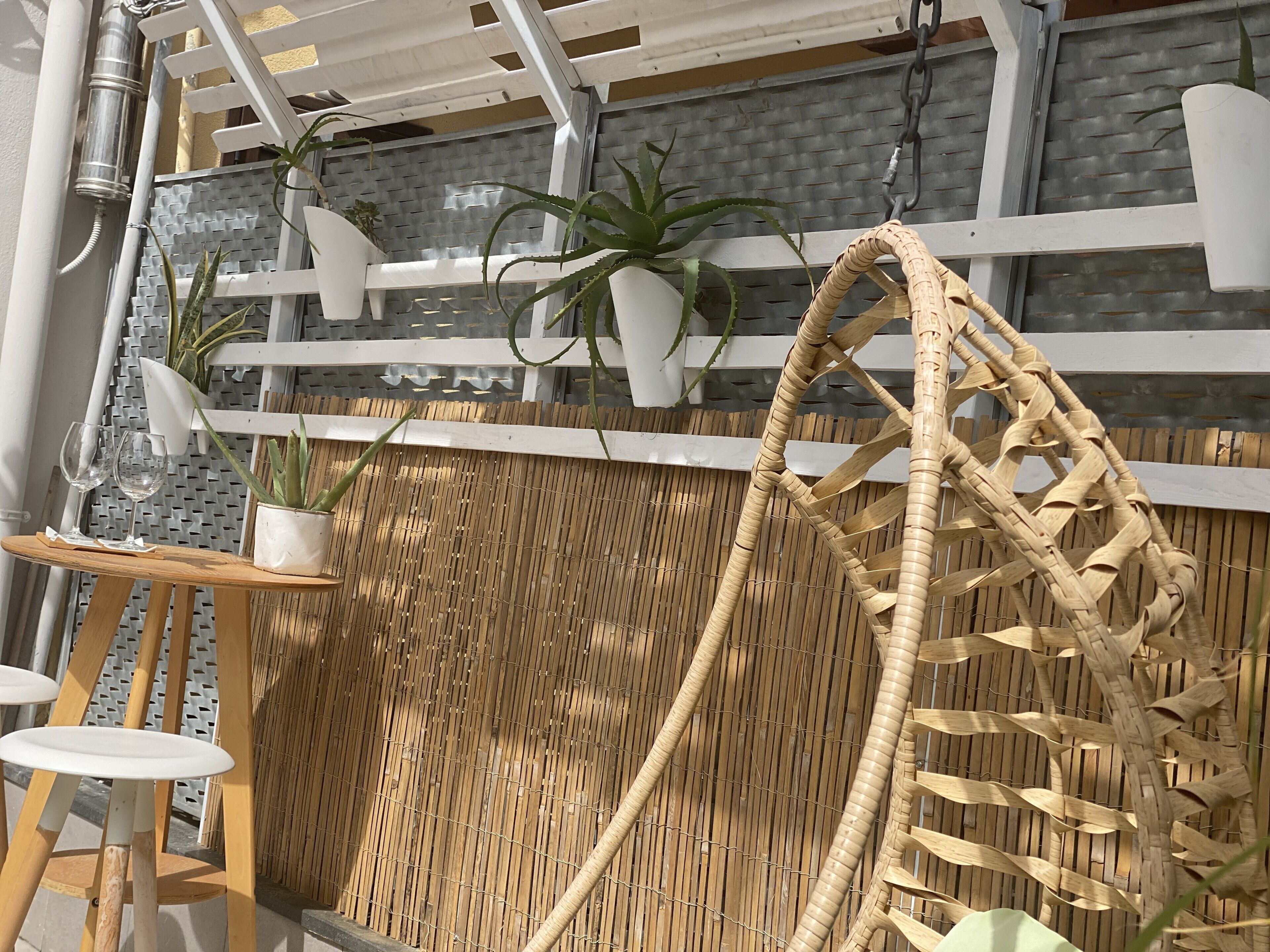 Une clôture en bambou, un fauteuil suspendu et des plantes en pot dans un espace patio.