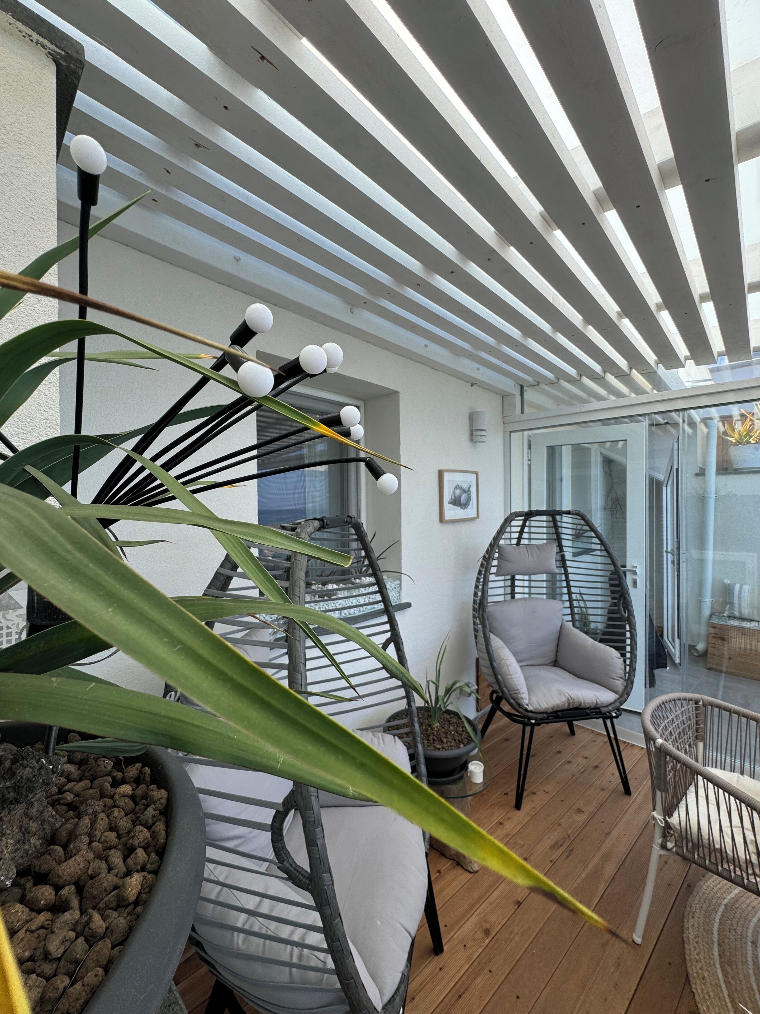Eine moderne Außenpatio mit Glastür zu einem Balkon, einem Hängekorbstuhl und einem Blumentopf.