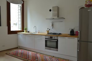 Una cocina moderna con armarios blancos, horno de acero inoxidable, estufa a gas y refrigerador.