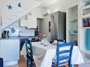 Una cucina moderna con mobili bianchi, un frigorifero in acciaio inossidabile e un'area pranzo con tovaglia bianca e sedie blu.