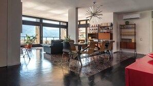 A spacious living area with a dining table, chairs, and a modern chandelier. There are potted plants and a bookshelf with books. - Terrace on the lake,private garage (Lugano)