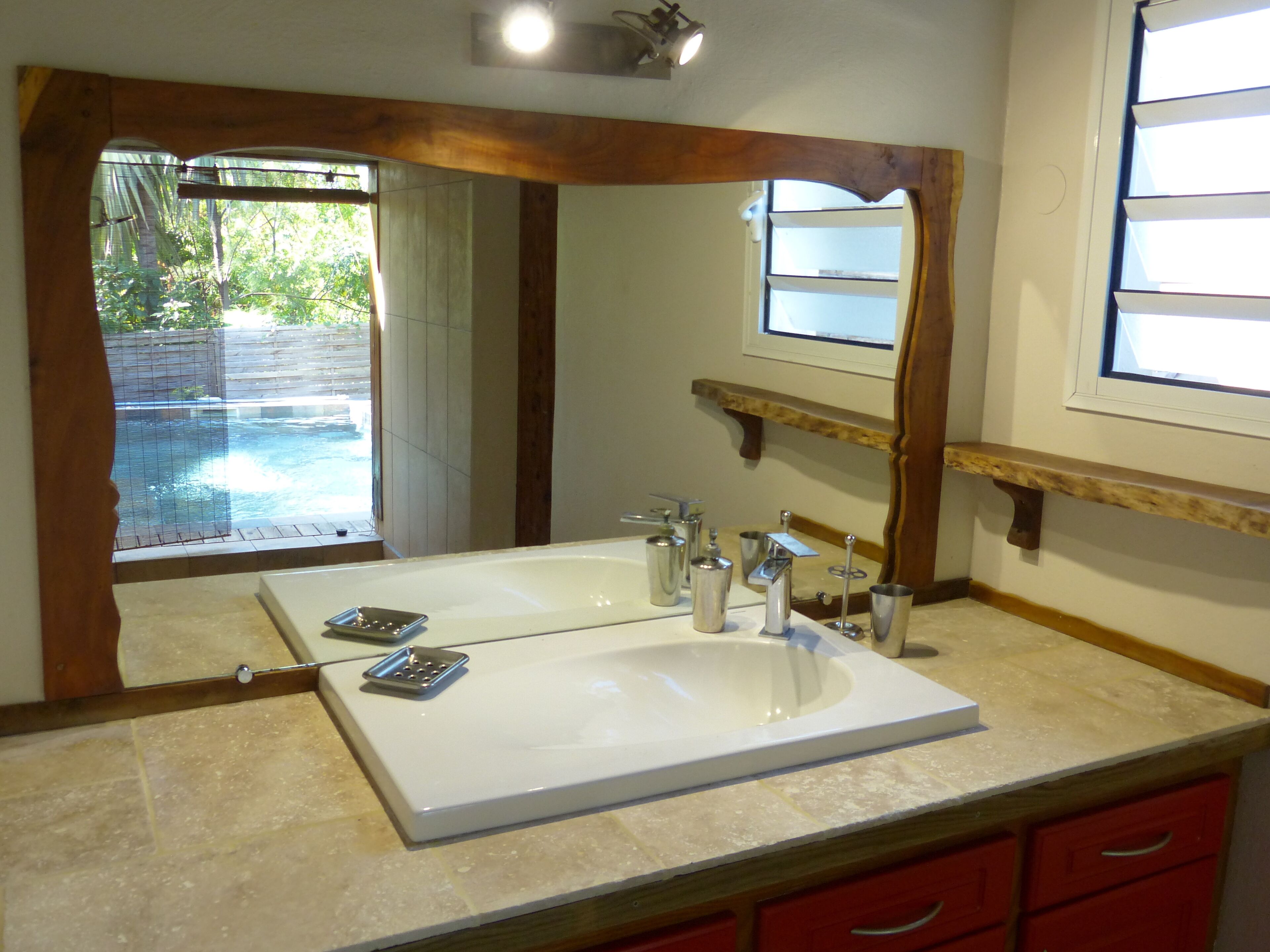 A bathroom with a large mirror, a white sink, and a wooden vanity.