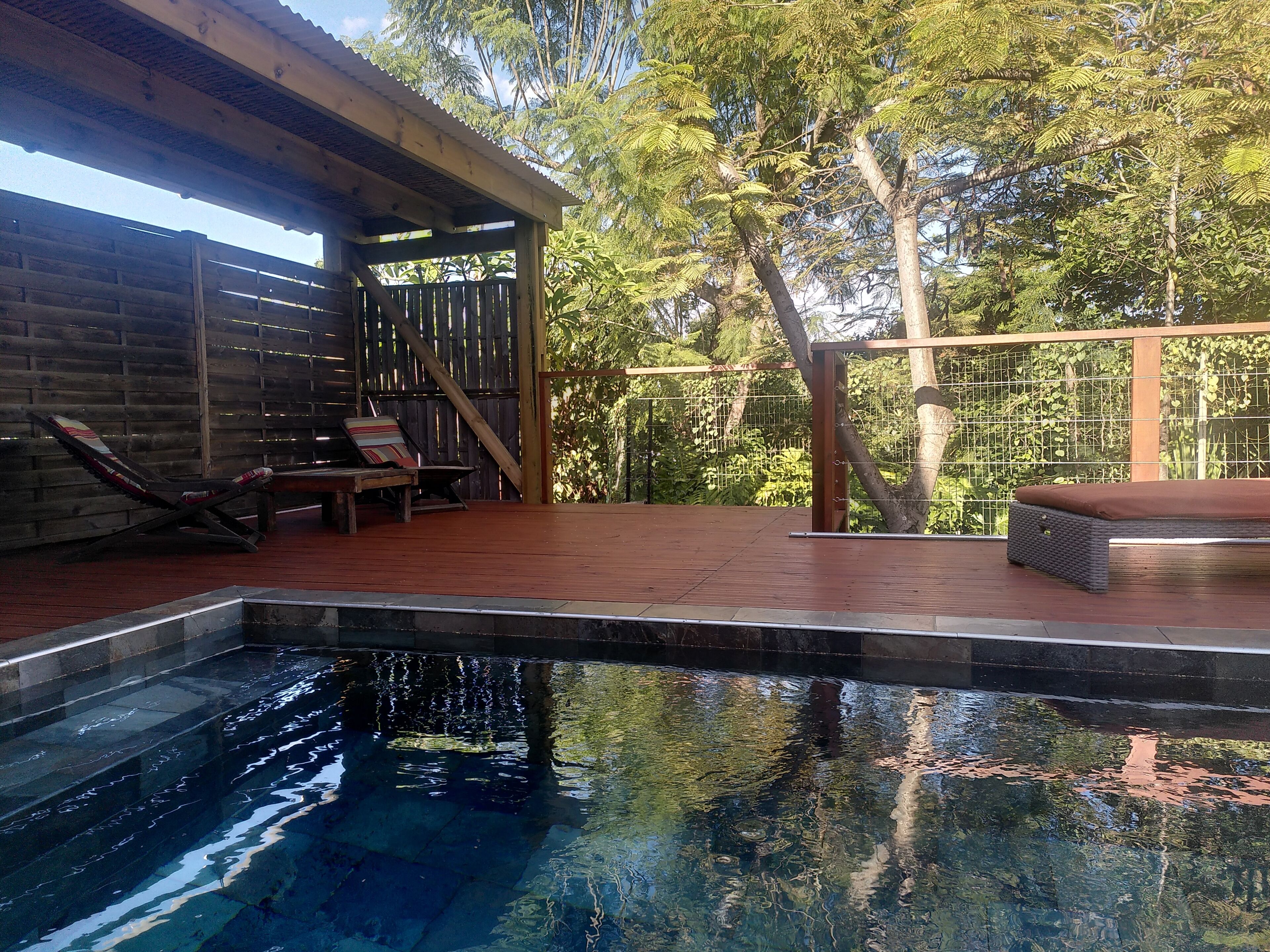 An outdoor swimming pool with a wooden deck, lounge chairs, and a covered seating area.