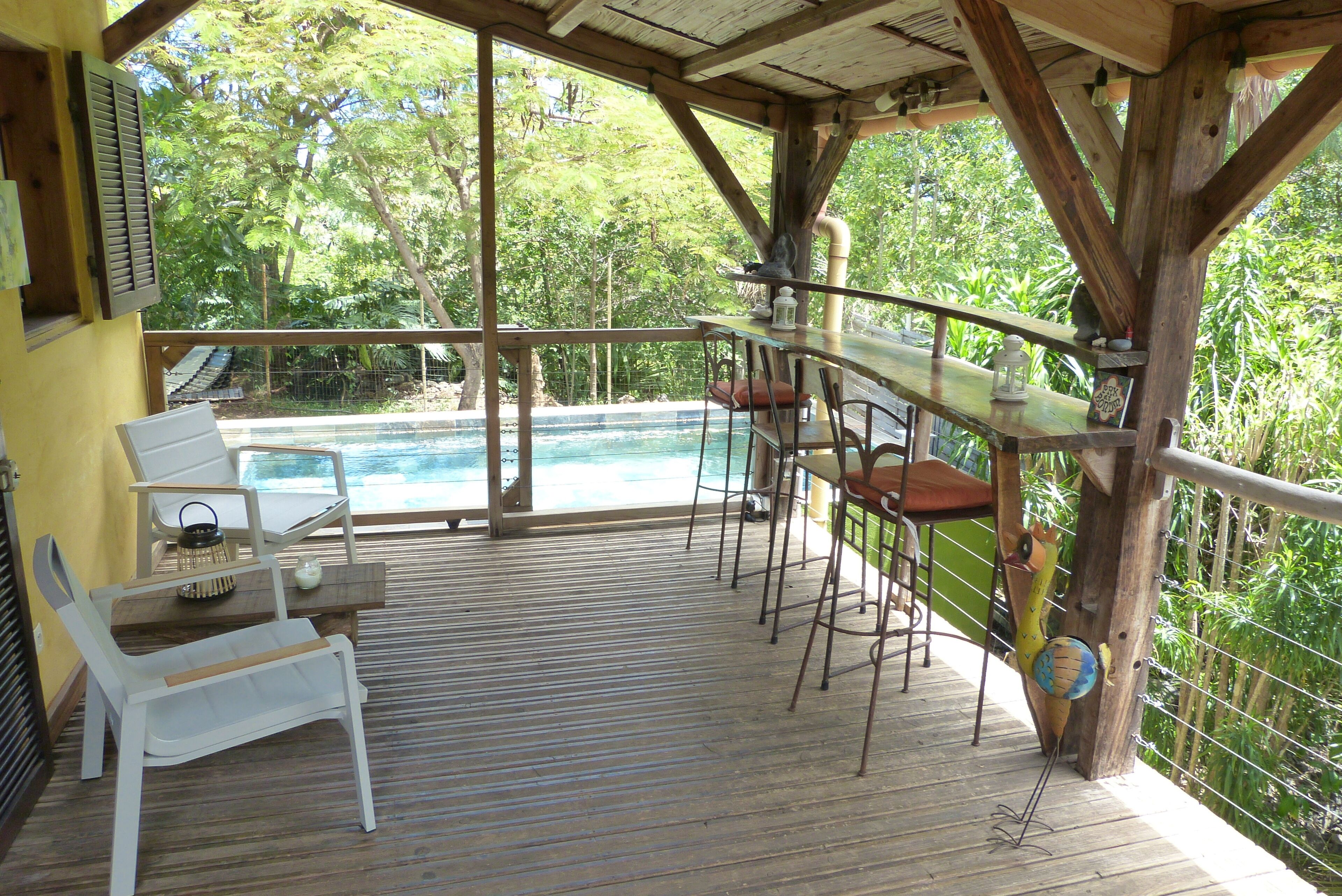 A wooden deck with a pool, white chairs, and a table with a lantern.