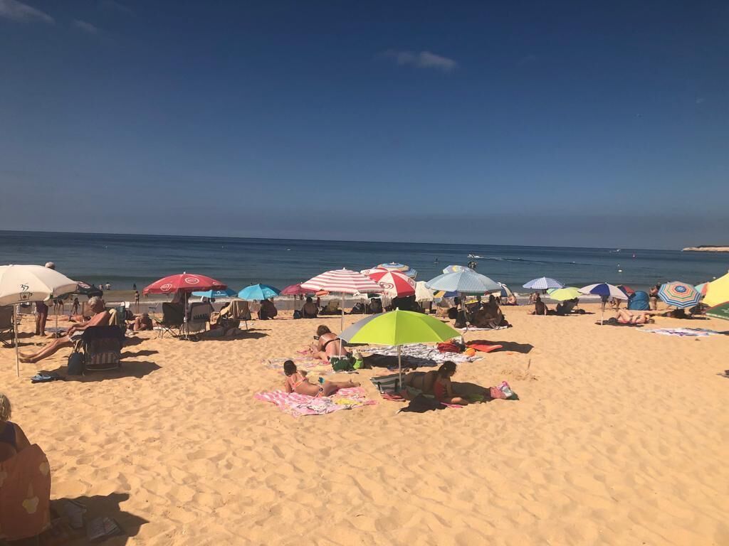 Ein Strand mit Menschen, die in der Sonne liegen und unter bunten Sonnenschirmen entspannen.