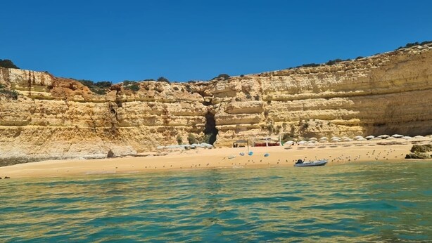 Eine Küstenlandschaft mit schichtartigen Klippen, einem Sandstrand und ruhigem Wasser.