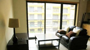 Ein Wohnzimmer mit einer Couch, einem Couchtisch und einer Lampe. Ein großes Fenster bietet Blick auf Gebäude.