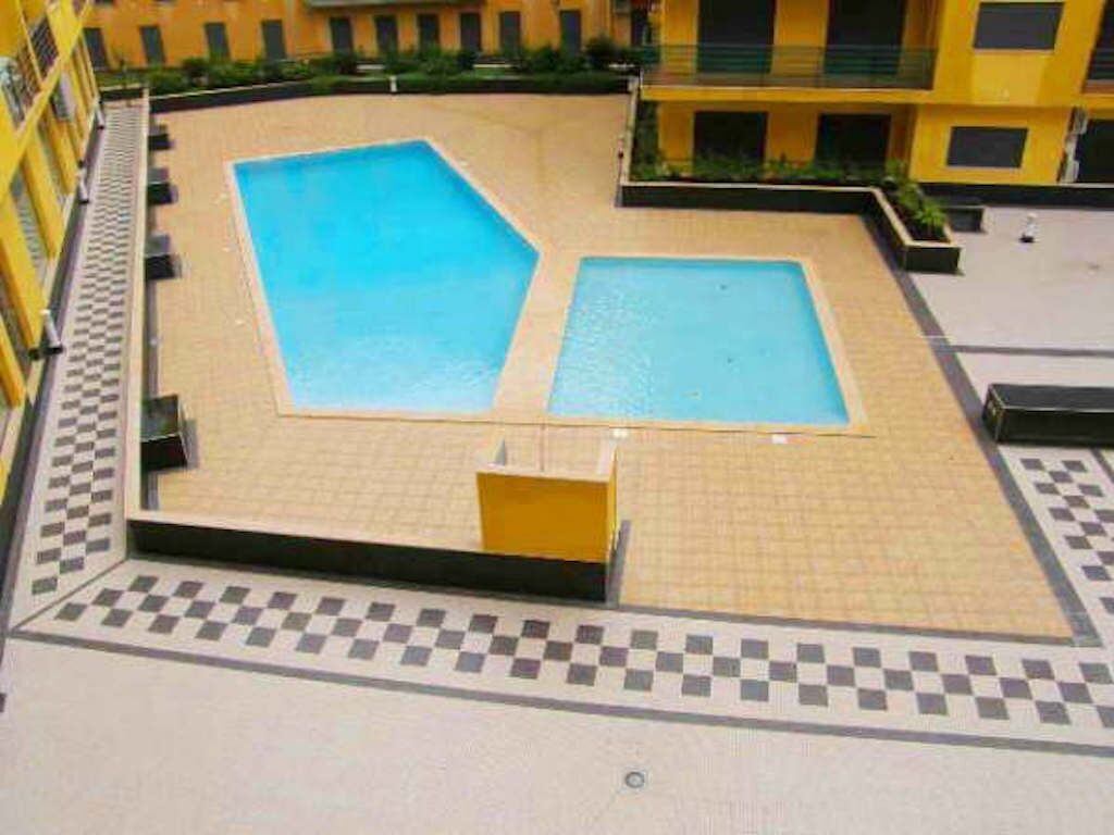 Une cour avec deux piscines, une bordure à carreaux et un bâtiment jaune en arrière-plan.