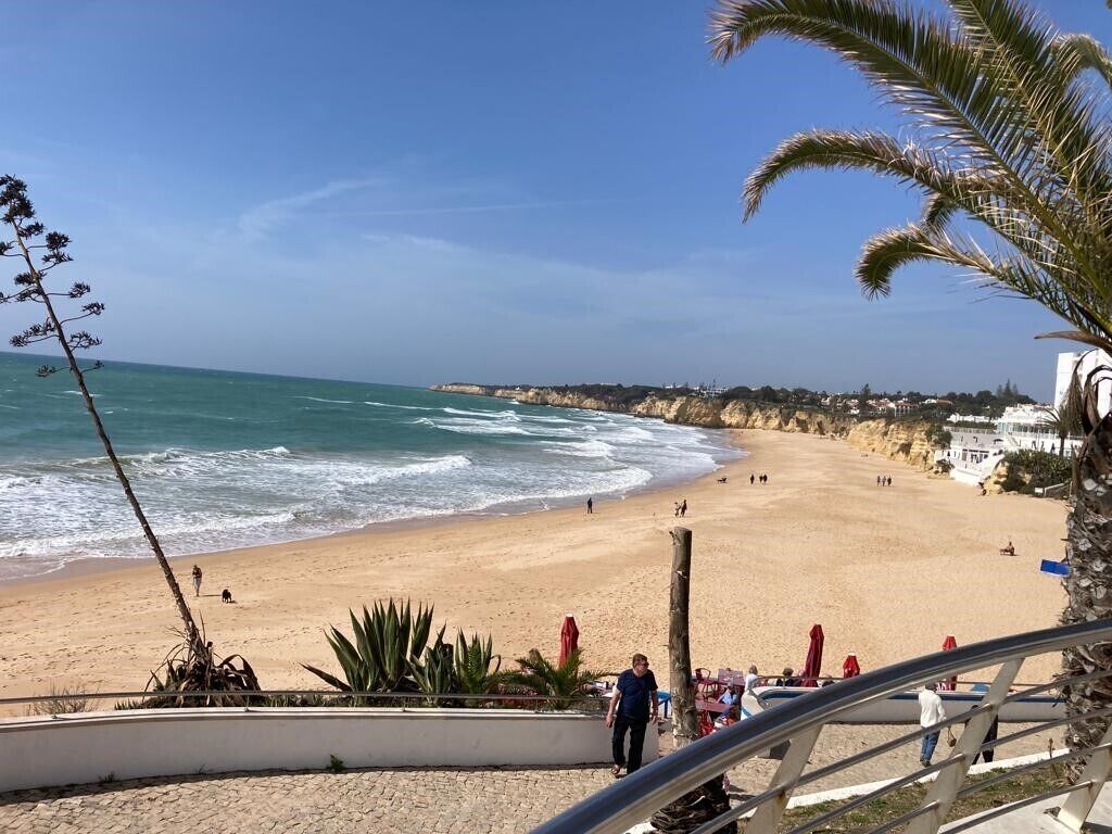 Ein Strand mit freiem Blick auf das Meer, sandigem Ufer und einigen Spaziergängern.