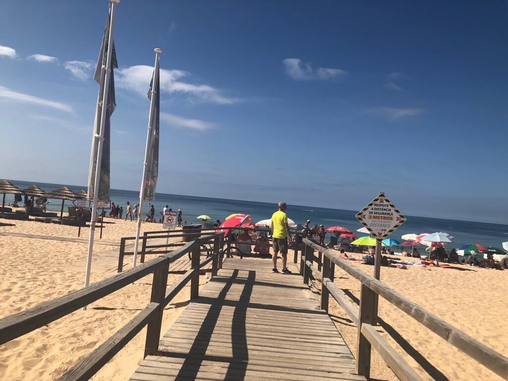 A wooden boardwalk leading to a beach with umbrellas and people.