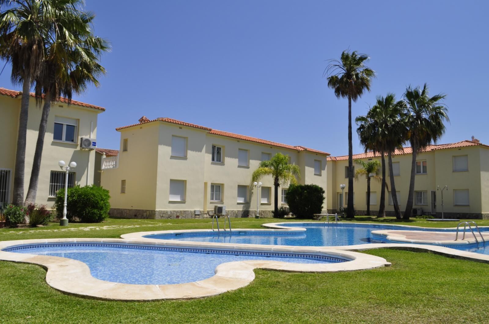 A hotel with a swimming pool, palm trees, and a clear blue sky.