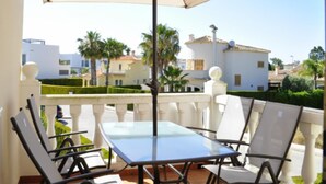 A patio with a glass table and four chairs, an umbrella, and a view of a residential area with houses and palm trees.