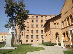 A courtyard with a statue, a large brick building with multiple windows, and a clear blue sky.