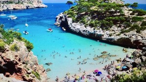 Une plage côtière bordée de falaises rocheuses, avec une eau turquoise cristalline et plusieurs bateaux ancrés à proximité.