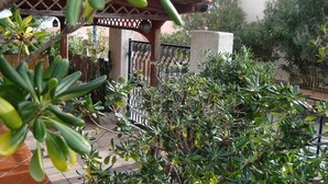 Ein überdachter Außenbereich mit einer Pergola, umgeben von üppigem Grün und einer gefliesten Terrasse.