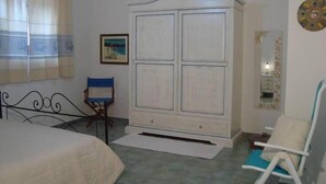 Ein Schlafzimmer mit einem Bett, einem Kleiderschrank, einem Sessel, einem Schreibtisch und einem Spiegel.