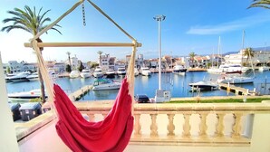 Ein Balkon mit einer roten Hängematte mit Blick auf einen Yachthafen, der Boote und Gebäude zeigt.