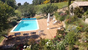 A rectangular swimming pool with a wooden deck, surrounded by lush greenery and flowers.