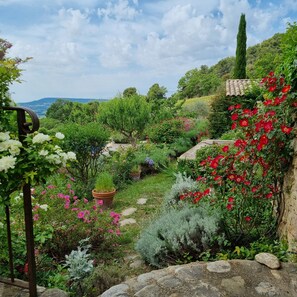 Un jardín con diversas plantas y flores, un muro de piedra y vistas del paisaje.