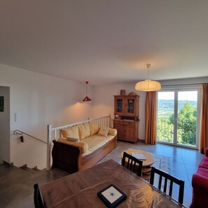 Ein Wohnzimmer mit einer Couch, einem Esstisch, einem Schrank und Blick ins Freie.