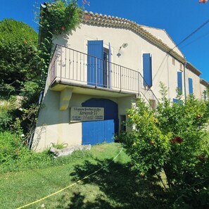 A two-story building with a balcony, a blue door, and a sign indicating a laundry service. - La Roseraie des Côtes Gite 4 places avec Piscine possibility 2 more beds (Vinsobres)