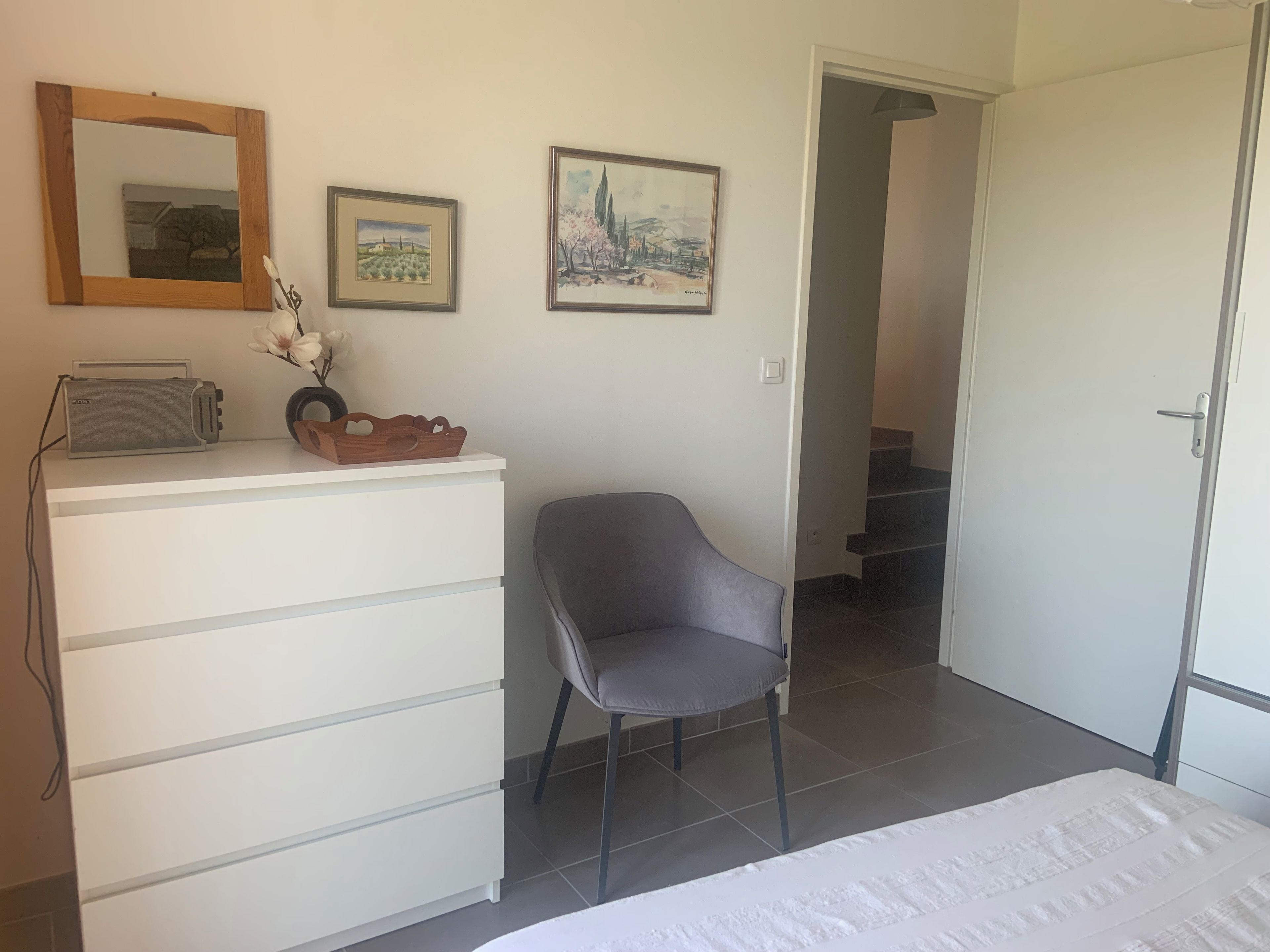 A hotel room with a bed, a desk with a toaster, a chair, and two framed pictures on the wall.