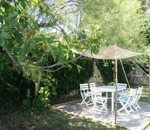Un patio al aire libre con mesa y sillas, rodeado de follaje y una pérgola.
