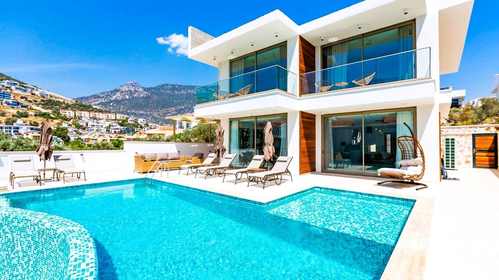 A modern two-story building with a rooftop pool, lounge chairs, and a view of the surrounding landscape.
