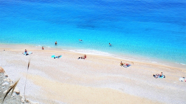 Ein Strand mit klarem, blauem Wasser und einem sandigen Ufer. Menschen entspannen sich in der Sonne und schwimmen.