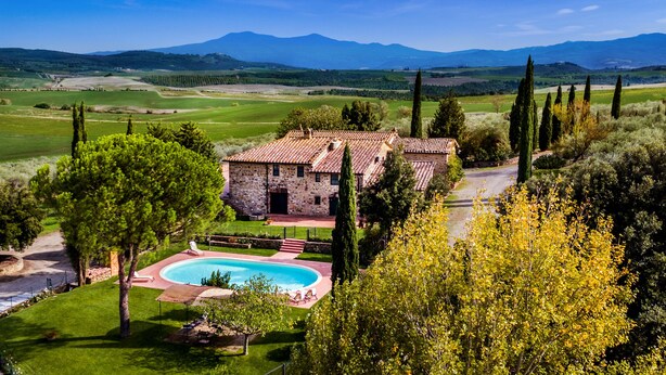 A stone villa with a swimming pool, surrounded by lush greenery and mountains in the background.