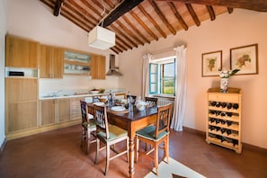 Une cuisine rustique avec des meubles de rangement en bois, une table à manger avec des chaises, un meuble à vin et une fenêtre avec des rideaux.