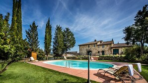A swimming pool with lounge chairs, a stone building, and tall trees in the background.