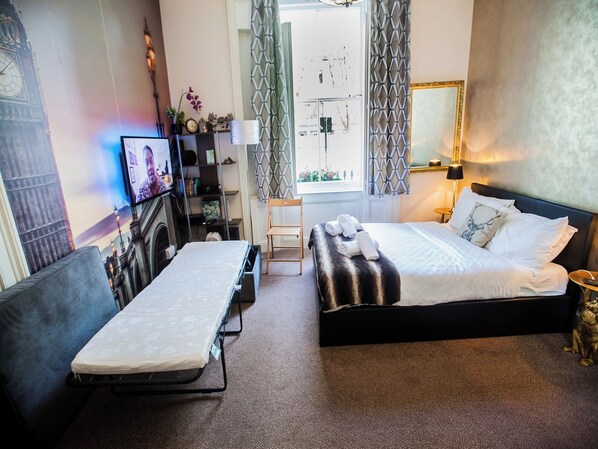 Une chambre d’hôtel avec un lit, un canapé, un bureau avec un ordinateur, une télévision et une fenêtre avec des rideaux.