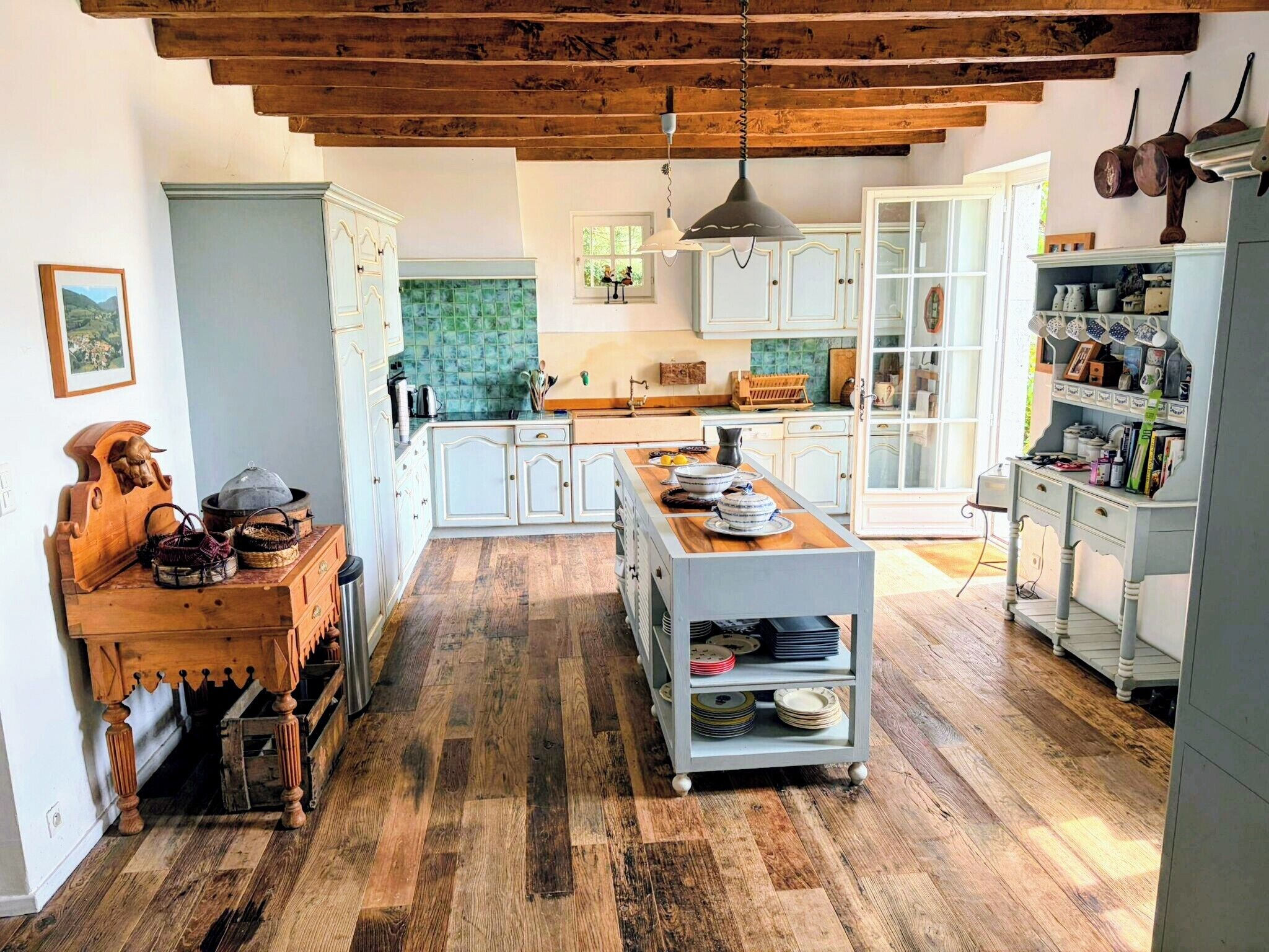 A spacious kitchen with wooden flooring, white cabinetry, and a central island with dishes.