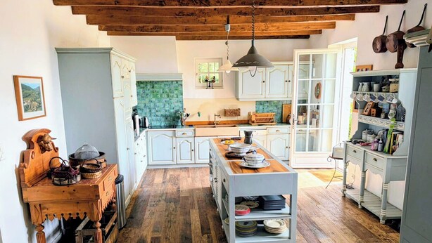 Une cuisine spacieuse dotée d’un plancher en bois, de meubles blancs et d’un îlot central où sont disposés de la vaisselle.