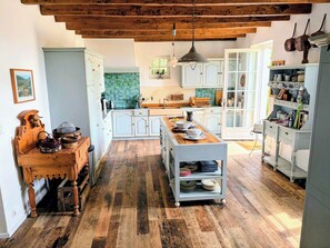 A spacious kitchen with wooden flooring, white cabinetry, and a central island with dishes.