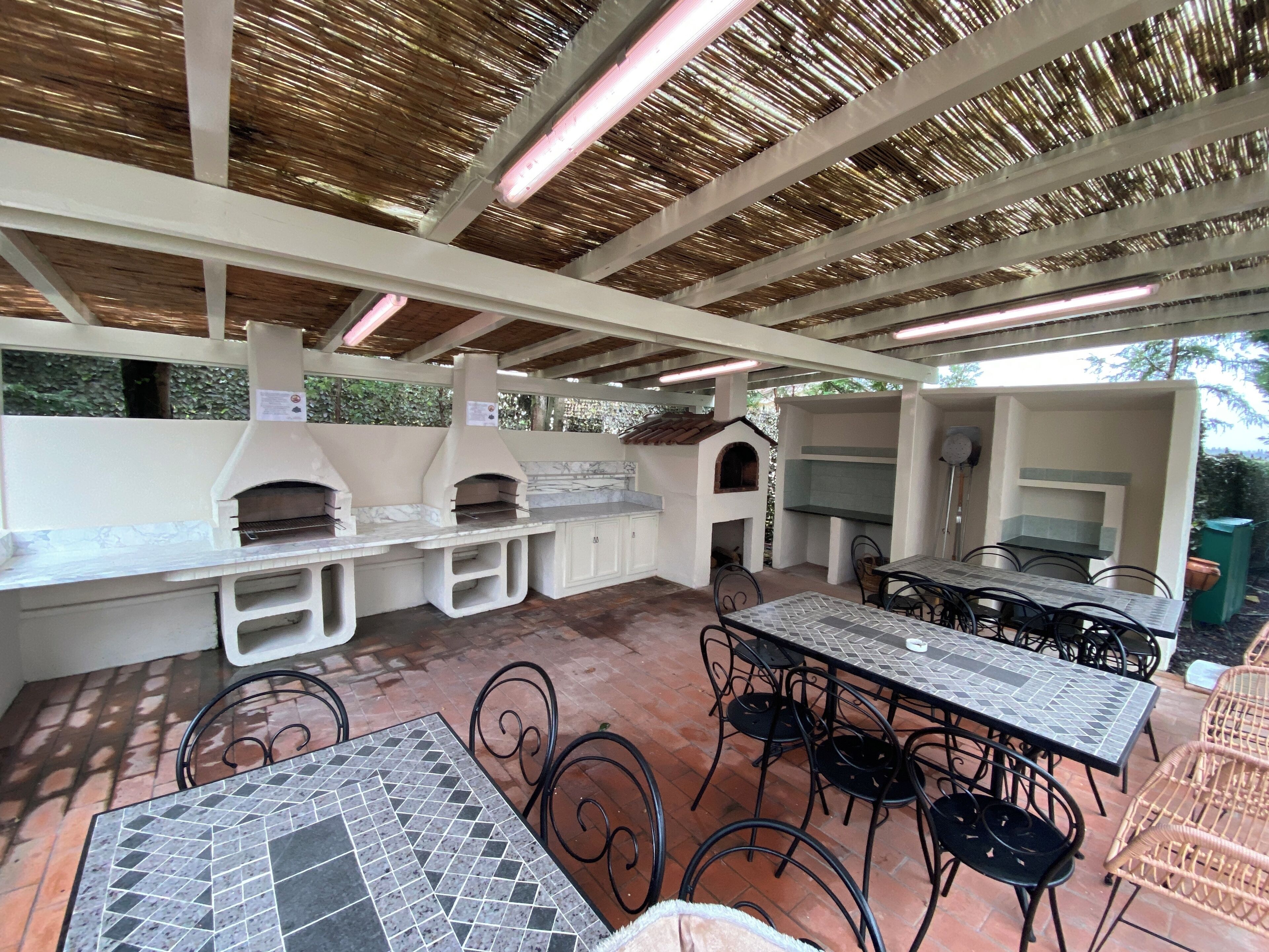 Un área de cocina al aire libre con una parrilla, horno para pizza y asientos de bar.