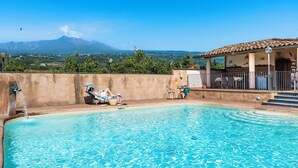 En swimmingpool med udsigt til et bjerg, en overdækket terrasse og en person, der slapper af ved poolen.