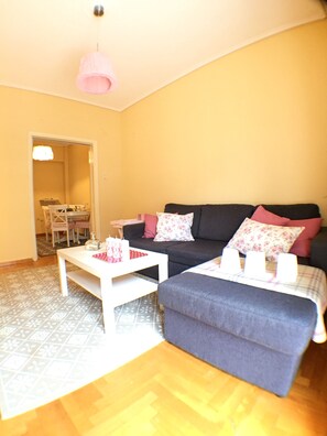 A living room with a sofa, a coffee table, and a dining area visible through an open door.