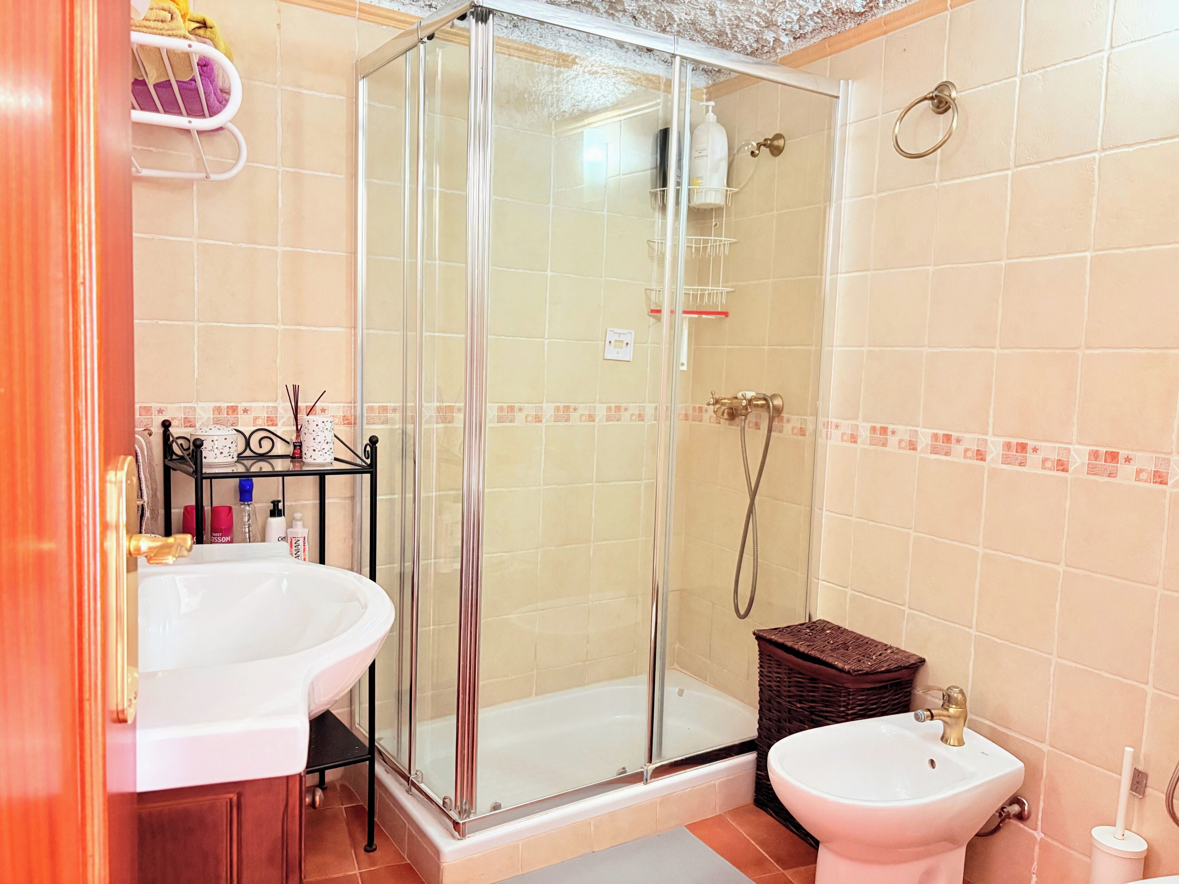 Een badkamer met een douchecabine van glas, een witte wastafel en een toiletbrons.